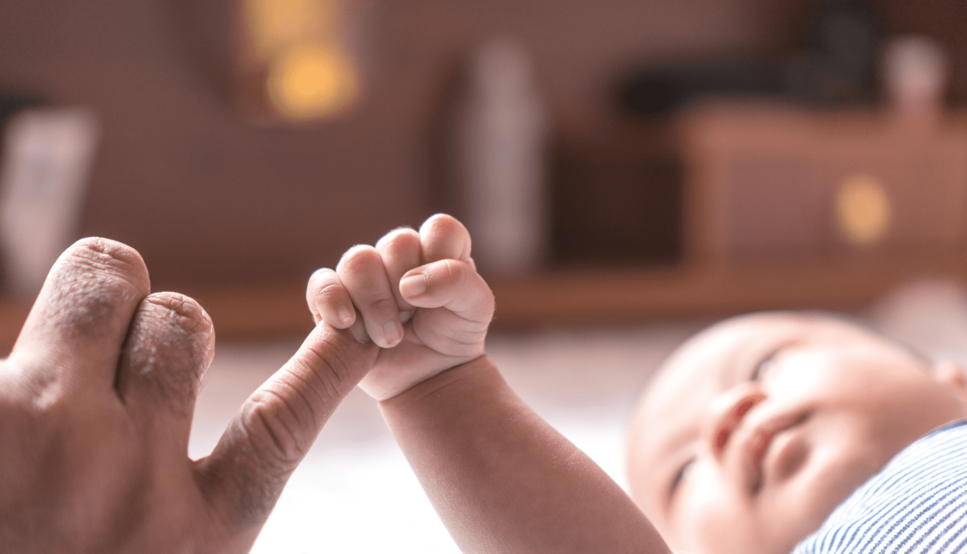 A man's hand gently cradling a baby's hand as they adjust to life with a new baby.