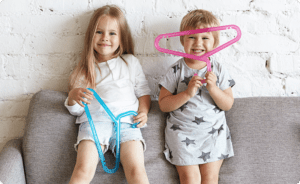 About Us: Two children sitting on a couch holding a pair of scissors.