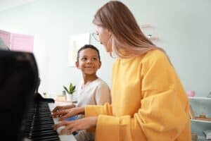 A woman providing music lessons to a boy, teaching him how to play the piano.