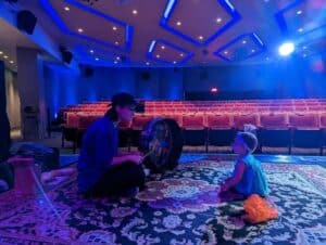 A woman and a child sitting on a rug in an auditorium, experiencing sensory sounds.