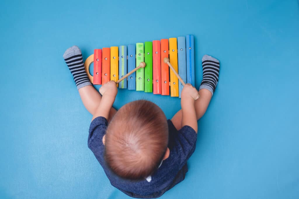 A baby is playing an xylophone on a blue background.