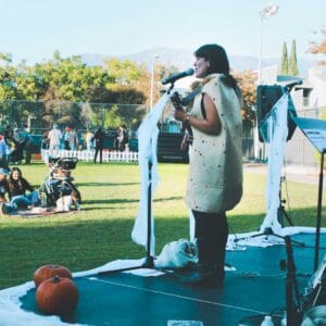 A woman singing on a stage in front of pumpkins, adding a touch of bop to her performance.