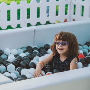 A little girl in sunglasses sitting in a ball pit, enjoying the whimsical atmosphere of Boo Bop.