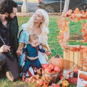 A man and woman pose with a baby in front of a pumpkin patch, creating a Boo-tiful family moment.