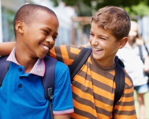 Two boys with backpacks smiling at each other.
