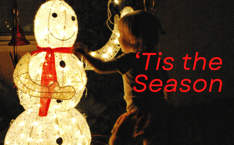 A young child running towards a light-up snowman with the words "'Tis the Season" overlaid